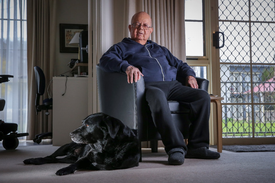 Twanny Farrugia sitting in a chair at home with his guide dog and companion Val.