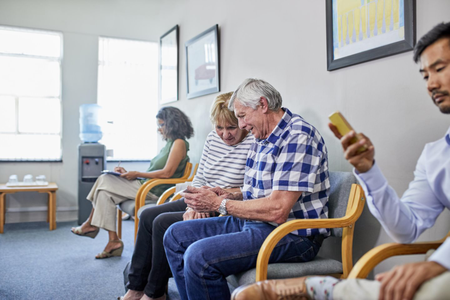 Senior couple using smart phone in clinic waiting room.