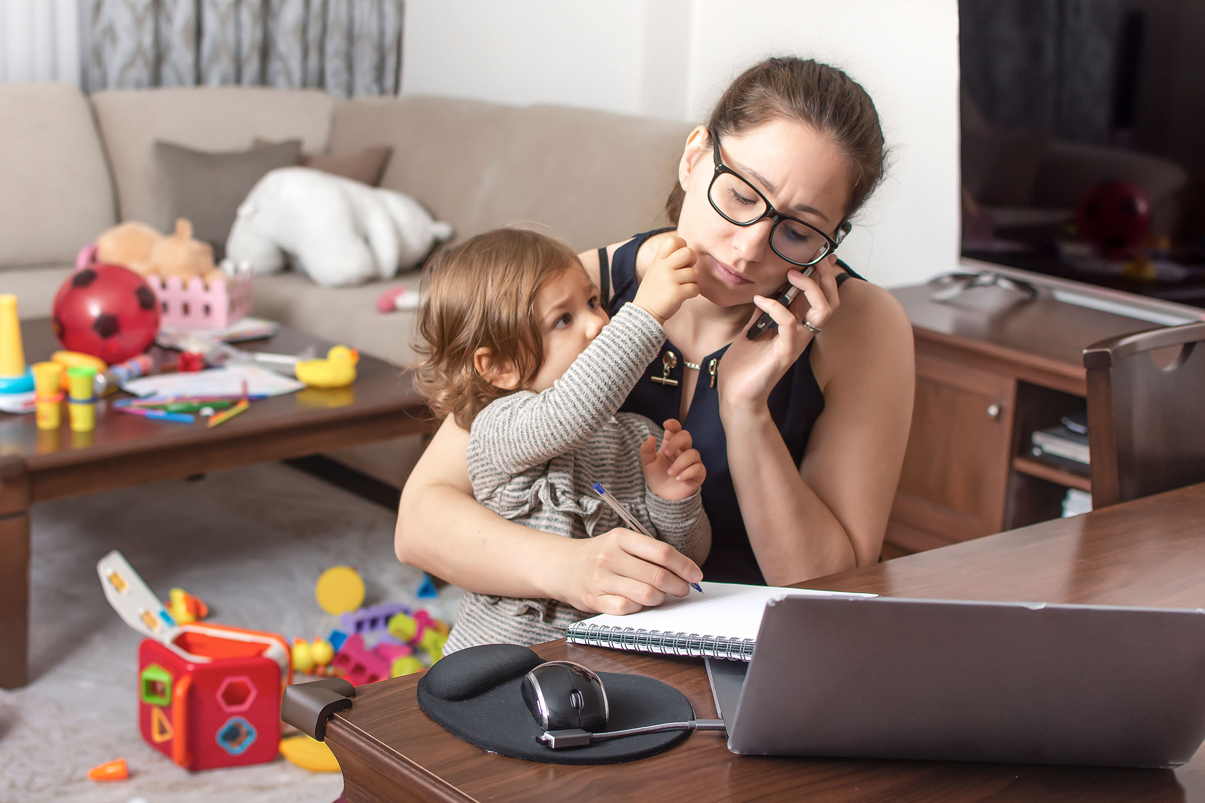 A young father working from home tries to make a phone call while his daughter plays with his computer.