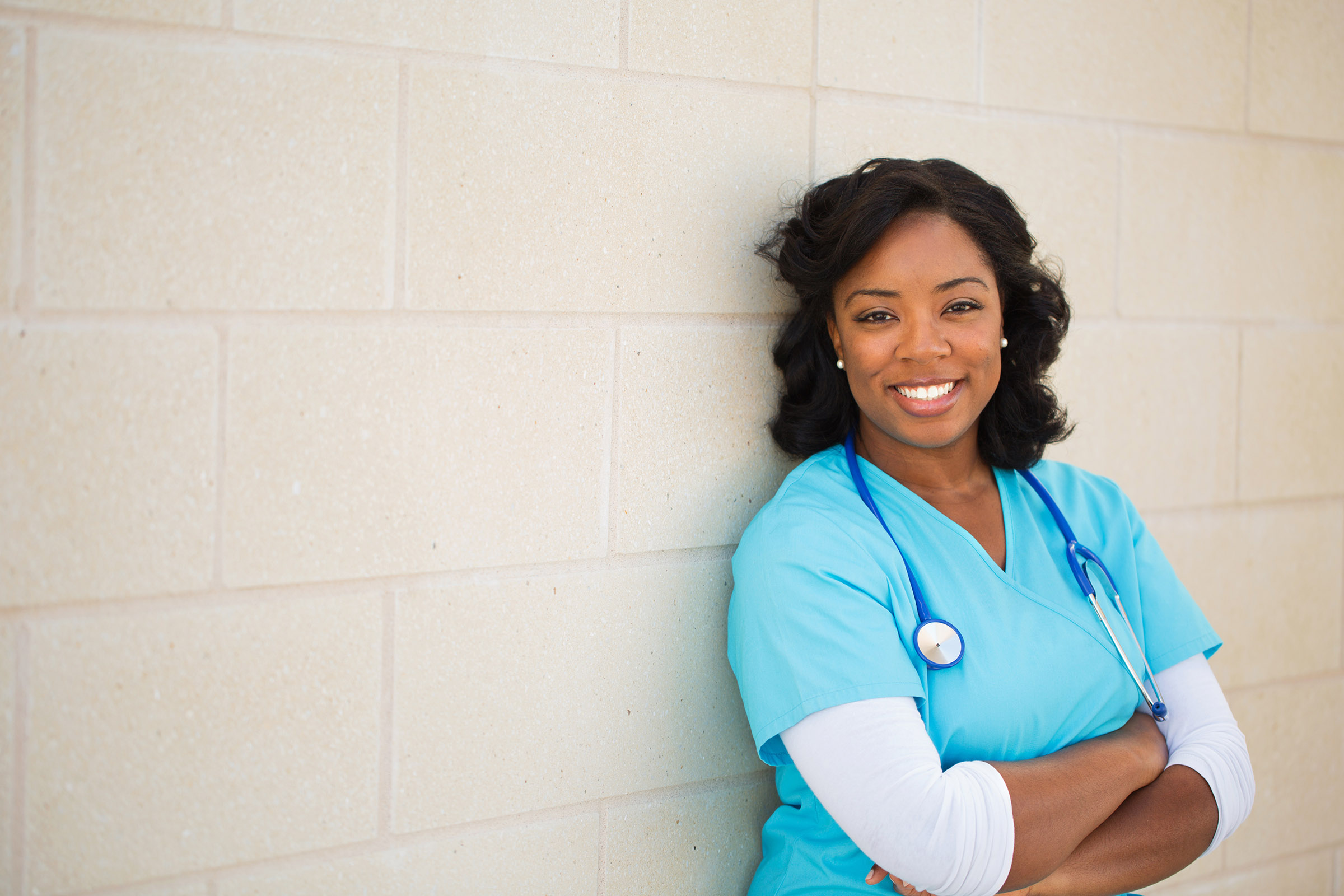 A smiling nurse leaning against a wall.