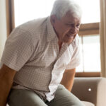 An aged care resident experiencing pain as he rises out of a chair.