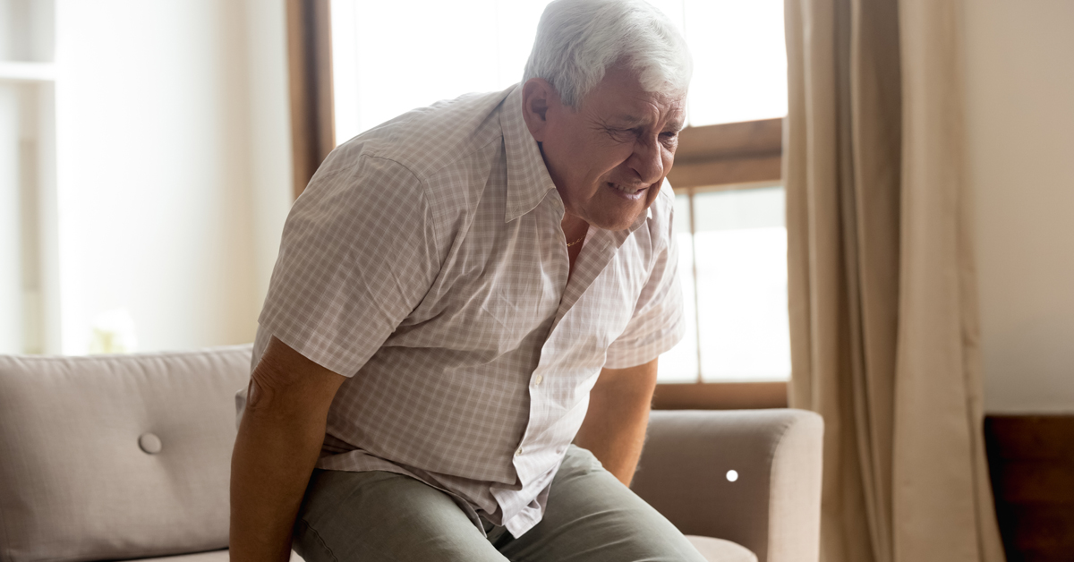 An aged care resident experiencing pain as he rises out of a chair.