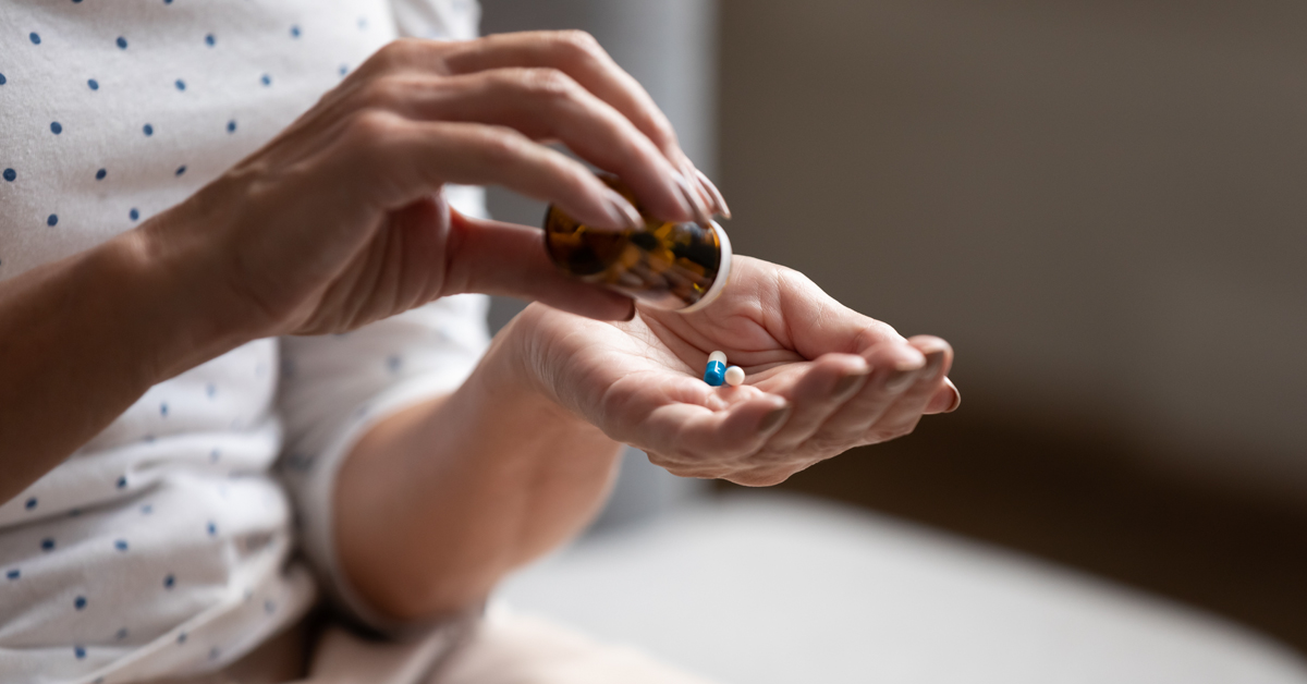 A person's hands extracting an antibiotic pill from a jar.