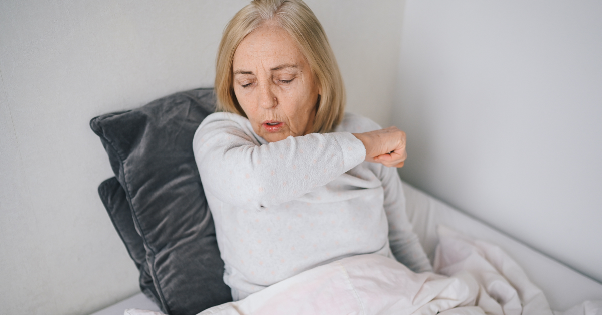 A woman with COVID-19 coughing while isolating at home.