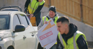 A tradesperson on a building site carrying a sign that says "final notice".