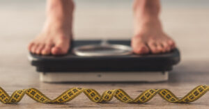 A person's feet on a scale with a tape measure in the foreground to represent body mass index.