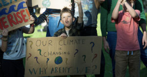 A young person at a climate change protest in Melbourne with a sign that reads "Our climate is changing, why aren't we?"