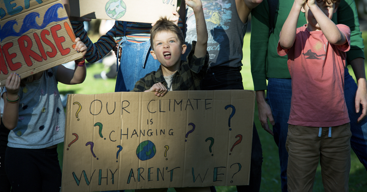 A young person at a climate change protest in Melbourne with a sign that reads "Our climate is changing, why aren't we?"