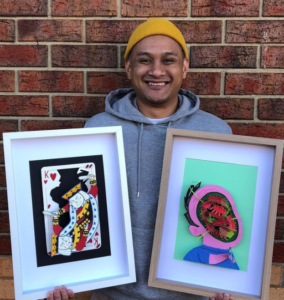 Artist Manny Sison standing and smiling with two of his artworks.