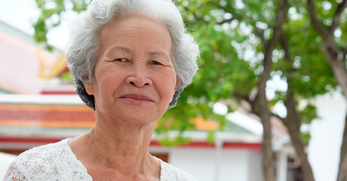 An older person outside in the sun with a tree in the background.