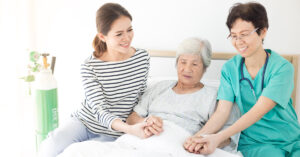 A nurse and a carer looking after an older patient in her bed and near the end of her life.