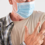 An older man displaying three fingers to represent the three doses of the COVID-19 vaccine he has received.