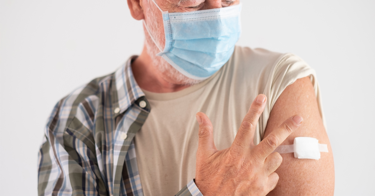 An older man displaying three fingers to represent the three doses of the COVID-19 vaccine he has received.