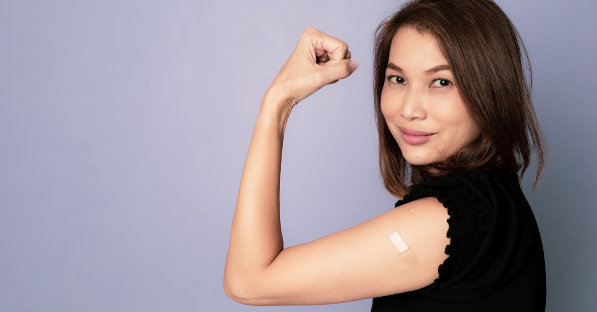 A woman smiling and showing off her bandaid after receiving a fourth COVID-19 vaccine dose.