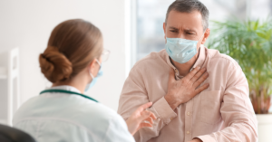 Man holding his chest with face mask on talking to a doctor