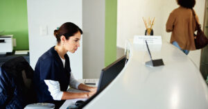 A female health professional works on a computer at a clinic