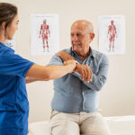 Physiotherapist helping senior man with elbow exercise in clinic.
