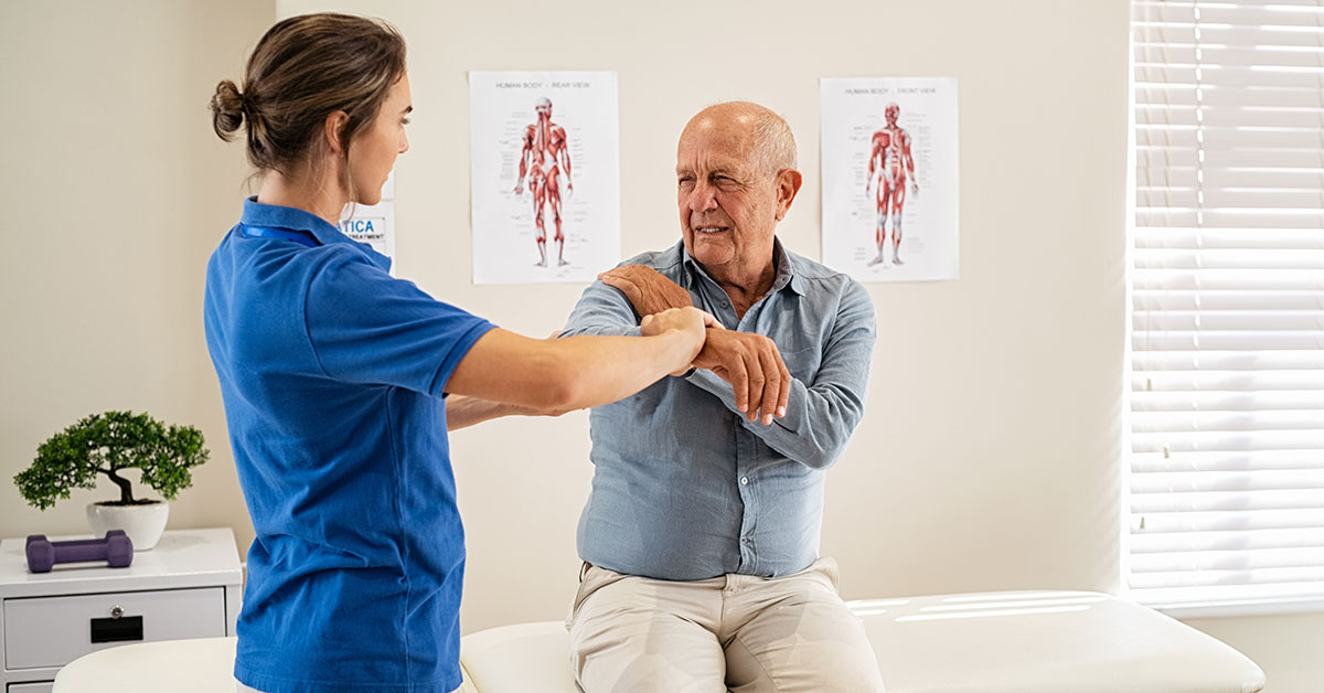 Physiotherapist helping senior man with elbow exercise in clinic.