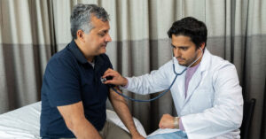 A doctor checks the heart-rate of his patient, a middle-aged man