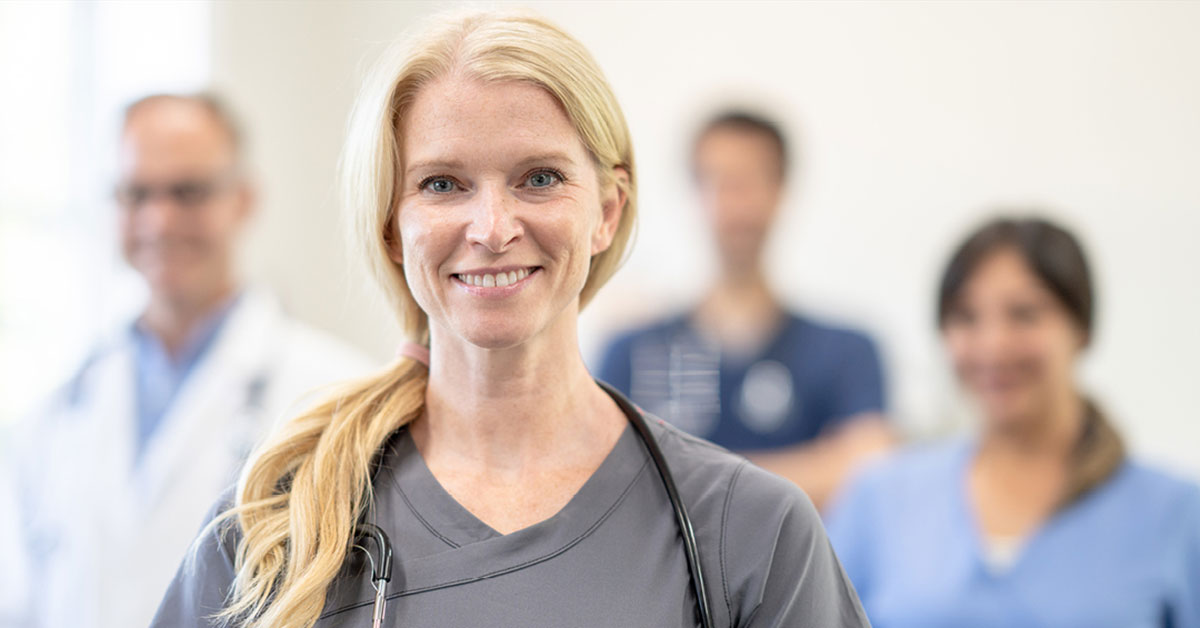 A female nurse smiles in front of other general practice staff