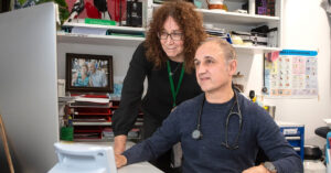 Dr Sam Zagarella, practice co-owner of Niddrie Medical, sits at a desk and looks at the computer alongside practice manager Megan Lay