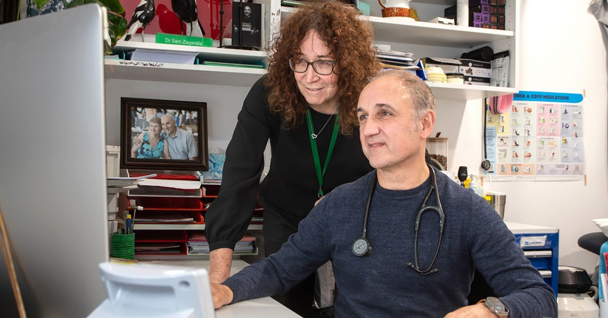Dr Sam Zagarella, practice co-owner of Niddrie Medical, sits at a desk and looks at the computer alongside practice manager Megan Lay