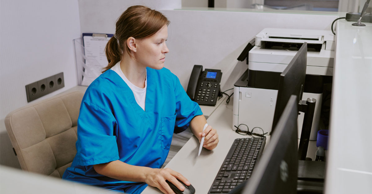 A practice nurse uses the recpetion computer at a general practice