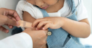 A doctor places a band aid over the upper arm of a young girl who had just received her flu vaccination