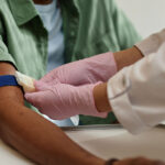 Close up image of nurse preparing patient for blood test and putting tourniquet on arm in procedure room at clinic.