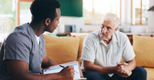 A young male nurse holding a clipboard speaks with a middle aged male patient