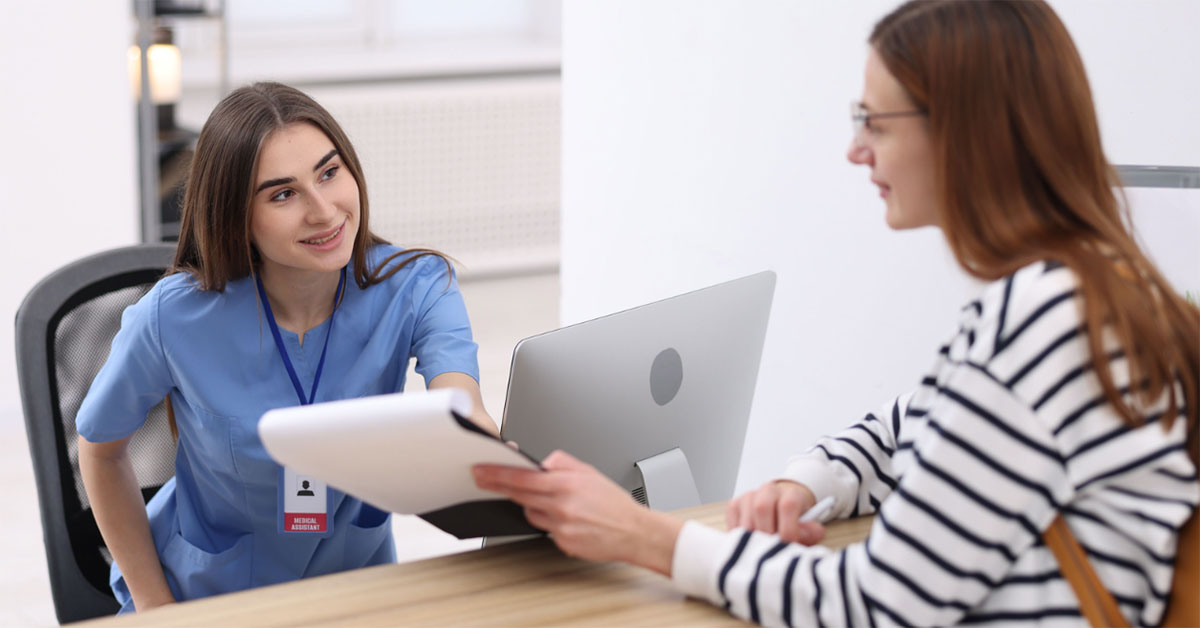 A clinical receptionist hands a patient a form to fill out