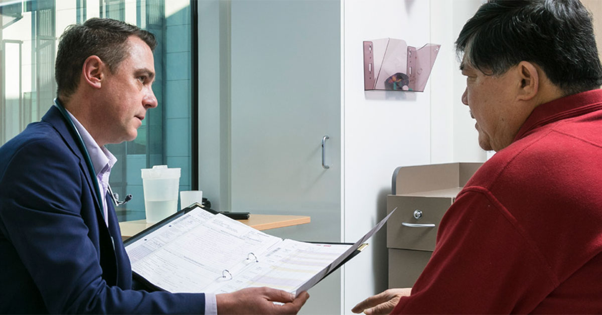 A male health professionals speaks with a middle aged male patient about a clinical trial