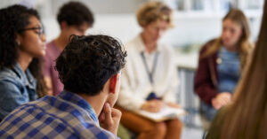 School students sit in a circle listening to a presenter.