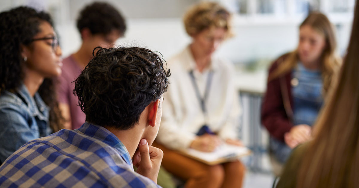 School students sit in a circle listening to a presenter.