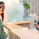 A clinician speaks with a male and female patient at the reception desk of a clinic
