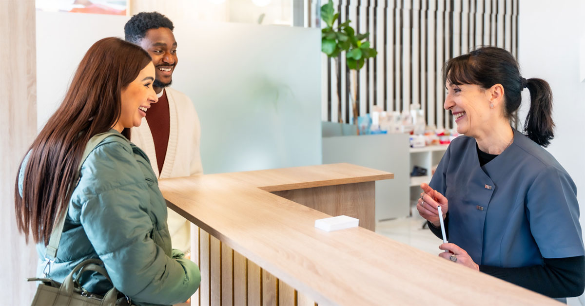 A clinician speaks with a male and female patient at the reception desk of a clinic