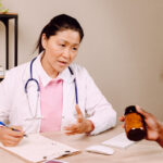 A female GP speaks to a female patient about some prescribed medicine in a bottle