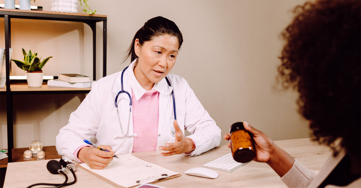 A female GP speaks to a female patient about some prescribed medicine in a bottle