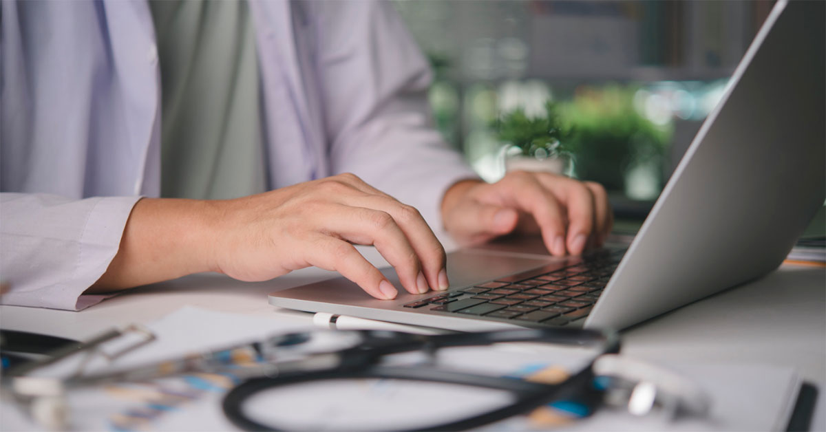 An unidentified general practitioner uses their laptop computer to make an eReferral for a patient