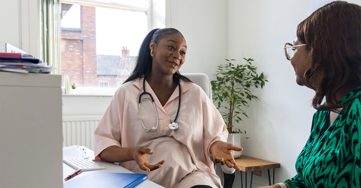 A female general practitioner sitting in her office speaks with a middle aged female patient
